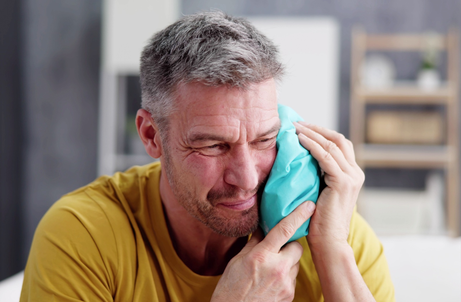 A man holding an ice pack to his jaw, appearing to be in discomfort, possibly due to TMJ disorder.
